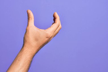 İzole edilmiş mor arka plan üzerinde parmaklarını gösteren beyaz bir adamın eli. Görünmez bir şeyi alıyor, parmakları boşluğu gösteren bir nesneyi tutuyor.