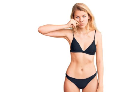 Bikini ağzı ve dudakları parmaklarıyla fermuar gibi kapalı olan güzel sarışın bir kadın. gizli ve sessiz, tabu konuşması 