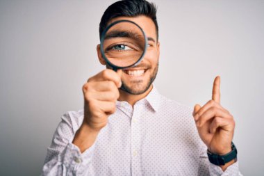 Genç dedektif, izole edilmiş arka planda büyüteçle bakıyor. Bir fikir ya da soru, mutlu yüzle işaret ediyor.