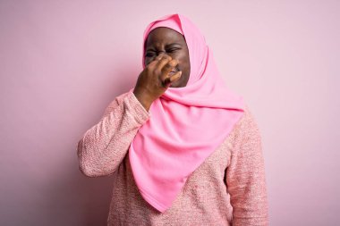 Genç Afro-Amerikan artı cüsseli kadın soyutlanmış pembe arka plan üzerine Müslüman başörtüsü takıyor pis ve iğrenç bir koku alıyor, nefesini burnu üzerinde tutuyor. Kötü kokuyor.