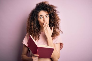 Kıvırcık saçlı, piercing 'li, pembe arka planda kitap okuyan, utancından ağzı açık, korkudan ağzı açık genç ve güzel bir bayan öğrenci.