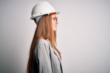 Beyaz arka planda güvenlik kaskı takan genç, güzel, kızıl saçlı bir mimar. Yan tarafa bakıyor, rahat bir görünüm sergiliyor. Kendine güvenen bir gülümsemesi var..