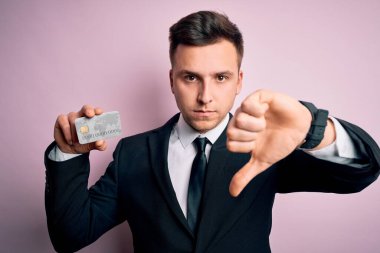 Yakışıklı beyaz iş adamı elinde pembe arka planda kredi kartı tutuyor. Kızgın bir yüzü var. Negatif işaretleri var.