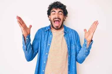 Kıvırcık saçlı ve ayı gibi sıradan kot ceket giyen yakışıklı genç adam başarı için çılgın ve çılgın bir kutlama yapıyor kolları havada ve gözleri kapalı heyecanla bağırıyor. Kazanan konsept 