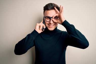 Genç, yakışıklı, beyaz bir adam akıllı telefondan konuşuyor, gülümsüyor ve gülümsüyor. Elleri gözlerinde, parmaklarından bakıyor.