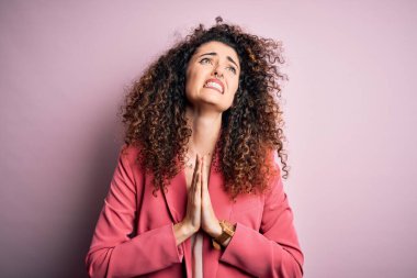 Kıvırcık saçlı ve piercingli genç ve güzel bir iş kadını zarif bir ceket giyiyor. Elleri bağlı yalvarıyor ve dua ediyor. Yüzünde umut ifadesi var. Yalvarıyorum..