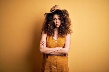 Güzel esmer kadın tatilde, kıvırcık saçlı ve piercingli, şapkalı, kuşkucu ve gergin, yüzünde çapraz kollu tasvip etmeyen bir ifade var. Negatif kişi.