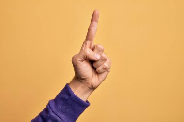 İzole edilmiş sarı arka planda parmaklarını gösteren beyaz bir gencin eli işaret parmağı kullanarak bir numarayı sayıyor, fikir ve anlayış gösteriyor.