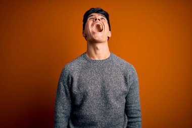 İzole edilmiş turuncu arka planda dikilen sıradan süveter giyen genç yakışıklı sinirli ve öfkeli çığlıklar atan, öfkeyle bağıran. Öfke ve agresif kavram.