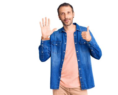 Genç ve yakışıklı bir adam gündelik giysiler giyer ve altı numaralı parmaklarını göstererek gülümserken kendinden emin ve mutlu olur.. 