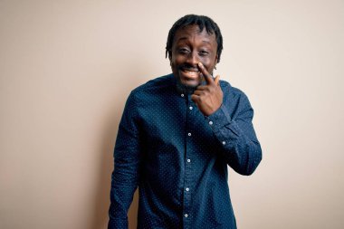 Beyaz arka planda duran, elleri ve burunları işaret eden, neşeli gülümseyen, gündelik gömlekler giyen genç, Afro-Amerikan bir adam. Güzellik konsepti