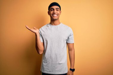 Yakışıklı Afro-Amerikan sporcusu sarı arka planda spor giysisi giyiyor. Gülümsüyor, avucunun içi kameraya bakıyor..