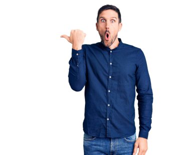 Gündelik tişört giyen genç ve yakışıklı bir adam elleri yana dönük, ağzı açık, şaşkın bir ifadeyle şaşırdı.. 