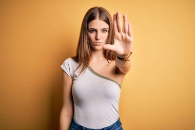 Güzel, kızıl saçlı bir kadın izole edilmiş sarı arka plan üzerine gündelik tişört giyip avucunun içi gibi şarkı söylemeyi kesiyor. Yüzünde olumsuz ve ciddi bir jest olan uyarı ifadesi.