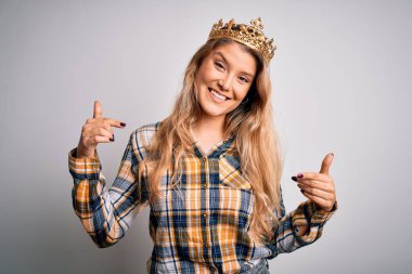 İzole edilmiş beyaz arka planda kraliçe tacı takan genç ve güzel sarışın bir kadın. Yüzünde bir gülümsemeyle, gururlu ve mutlu parmaklarıyla kendini işaret ediyor..