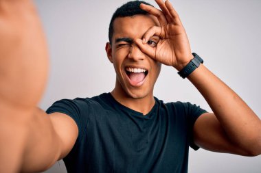 Genç, yakışıklı, Afro-Amerikalı, günlük tişörtler giymiş, mutlu yüzlü, mutlu yüzüyle selfie çeken, el pençe divan duran, el pençe divan duran bir adam.