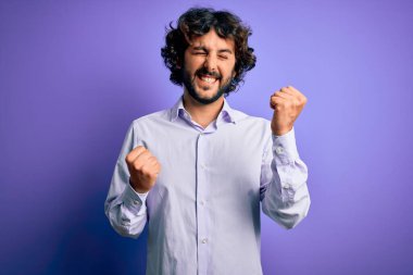 Mor arka plan üzerinde duran sakallı yakışıklı iş adamı kolları havada ve gözleri kapalı bir şekilde başarıyı kutluyor ve şaşırıyor. Kazanan konsept.