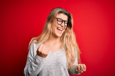 Gözlüklü, süveter ve gözlüklü genç ve güzel bir kadın başarının heyecanı içinde kollarını kaldırmış ve gözleri kapalı zaferi kutluyor. Kazanan konsept.