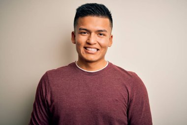 Yüzünde mutlu ve havalı bir gülümsemeyle izole edilmiş beyaz arka planda dikilen gündelik süveter giyen genç, yakışıklı latin adam. Şanslı kişi..