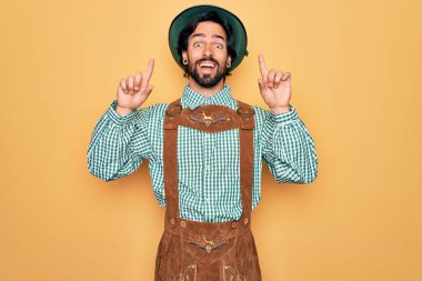 Almanya festivali için geleneksel Alman Ekim Festivali kıyafeti giyen genç yakışıklı adam şaşırmış, şaşırmış ve parmaklarıyla işaret ediyor ve kollarını kaldırıyordu..