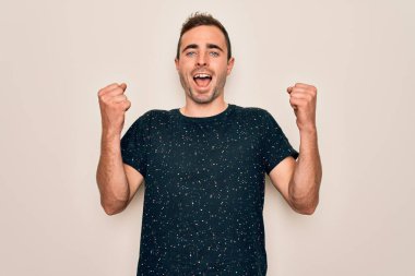 Mavi gözlü genç bir adam beyaz arka plan üzerinde dikilmiş kollarını kaldırarak ve açık gözlerle başarıyı kutluyor ve şaşırıyor. Kazanan konsept.