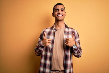 Sarı arka plan başarısı tabelasının üzerinde dikilmiş, gülümseyen ve mutlu genç ve yakışıklı Afro-Amerikalı bir adam. Neşeli ifade ve kazanan jest.