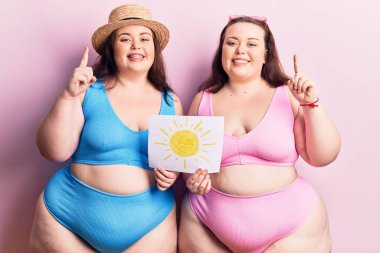 Bikini giyen, güneş çeken, gülümseyen, mutlu yüzlü, soru soran genç ve büyük beden ikizler. 