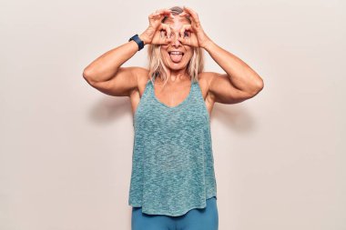 Orta yaşlı beyaz kadın spor kıyafetleri giyiyor dürbün gibi jest yapıyor dili dışarı çıkarıyor, gözleri parmaklarından bakıyor. çılgın ifade. 