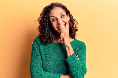 Orta yaşlı, süveter giyen güzel bir kadın kameraya kolları çapraz ve çenesi açık gülümsüyor. Olumlu düşünmek. 