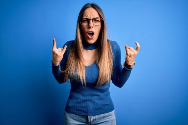 Mavi gözlüklü, genç, sarışın bir kadın mavi arka planda durup çılgın bir ifadeyle elleri havada rock sembolü yaparken bağırıyor. Müzik yıldızı. Ağır konsept.