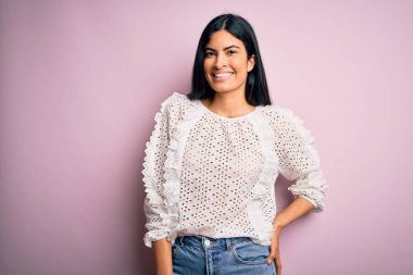 Moda kıyafetleri giyen genç ve güzel bir kadın. Manken, sokak tarzı giyiniyor. Pembe arka planda dikiliyor.