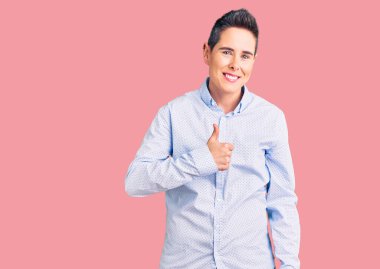 Kısa saçlı, iş kıyafetleri giyen, el hareketleriyle mutlu bir jest yapan genç bir kadın. Kameraya bakıp başarıyı gösteren ifade. 