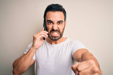 Sakallı genç yakışıklı adam akıllı telefonda konuşuyor sinirlenmiş ve sinirlenmiş bir şekilde bağırıyor, çıldırmış ve el kaldırarak bağırıyor.