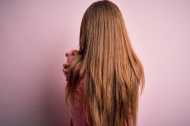 Genç, güzel, kızıl saçlı bir kadın pembe arka planda rahat bir süveter giyiyor. Kendine mutlu ve pozitif bir şekilde sarılıyor. Sevgi ve özgüven.