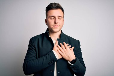 Zarif bir kışlık ceket giyen genç yakışıklı iş adamları izole edilmiş arka planda duruyor. Elleri göğsünde, gözleri kapalı ve yüzünde minnet dolu bir jest ile gülümsüyor. Sağlık kavramı.