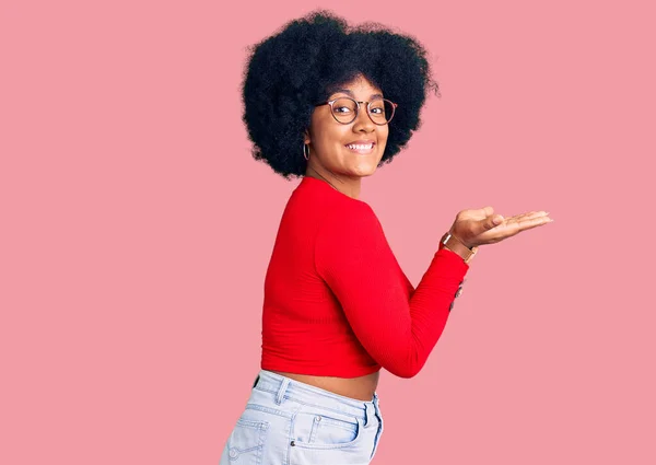 年轻的非洲裔美国姑娘 身穿休闲装 戴着眼镜 两手张开手掌 展示着复制的空间 脸上挂着广告的笑容 高兴极了 — 图库照片