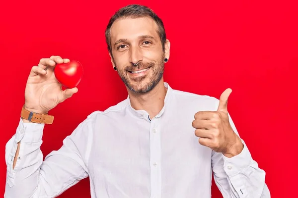 Joven Hombre Guapo Sosteniendo Corazón Sonriendo Feliz Positivo Pulgar Hacia — Foto de Stock