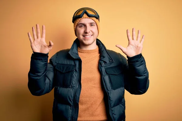 年轻英俊的高加索男子 戴着帽子 外套和滑雪眼镜 在冬雪天气里 他带着自信和快乐的笑容 用手指指指着十号 — 图库照片