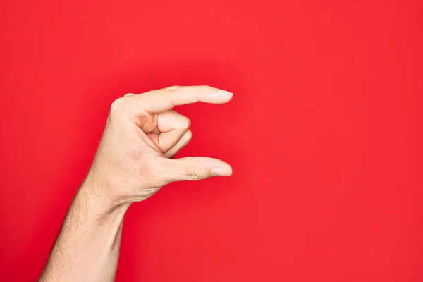 Hand of caucasian young man showing fingers over isolated red background picking and taking invisible thing, holding object with fingers showing space