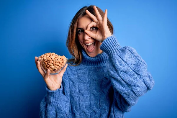 Young Beautiful Brunette Woman Holding Bowl Peanuts Blue Background Happy — Stock Photo, Image