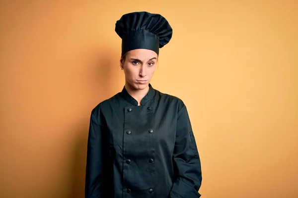 Young beautiful chef woman wearing cooker uniform and hat standing over yellow background skeptic and nervous, frowning upset because of problem. Negative person.