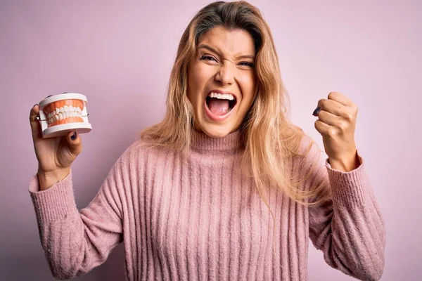 Jovem Bela Mulher Loira Segurando Dentadura Plástico Sobre Fundo Rosa — Fotografia de Stock