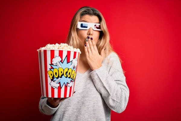 Young beautiful blonde woman watching movie using 3d glasses eating popcorns cover mouth with hand shocked with shame for mistake, expression of fear, scared in silence, secret concept