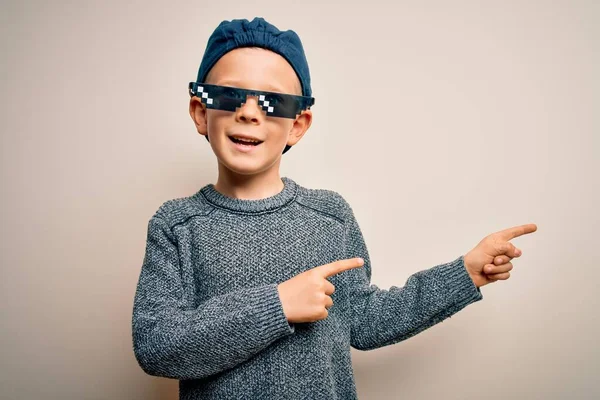 Young little caucasian kid wearing internet meme thug life glasses over isolated background smiling and looking at the camera pointing with two hands and fingers to the side.