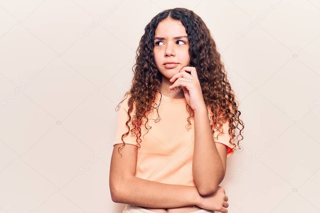 Beautiful kid girl with curly hair wearing casual clothes serious face thinking about question with hand on chin, thoughtful about confusing idea 