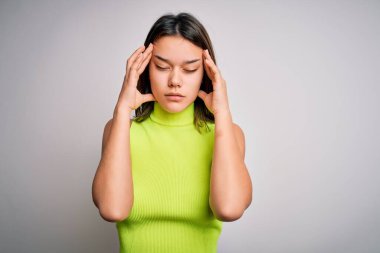 Genç, güzel, esmer bir kız izole edilmiş beyaz bir arka plan üzerine günlük tişört giyiyor ve stresten dolayı baş ağrısı çekiyor. Migren ağrısı..