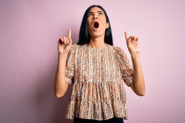 Pembe arka planda zarif bir stil takan genç, güzel İspanyol moda kadını şaşırmış ve şaşırmış bir şekilde başımı kaldırıp parmaklarımı gösterip kollarımı kaldırdım..