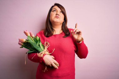 Güzel ve iri bir kadın pembe arka planda romantik laleler tutuyor üzgün ve üzgün görünüyor, parmaklarıyla yönü gösteriyor, mutsuz ve depresif..