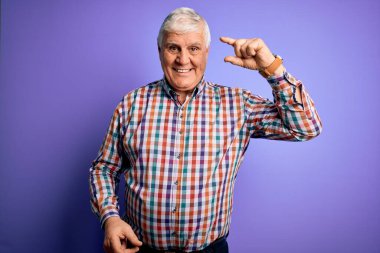 Üst düzey yakışıklı beyaz adam, izole edilmiş mor arka planda sıradan bir gömlek giyiyor gülümsüyor ve kendine güvenen el hareketleriyle küçük boy işareti yapıyor, parmaklarıyla bakıyor ve kameraya bakıyor. Ölçü kavramı.