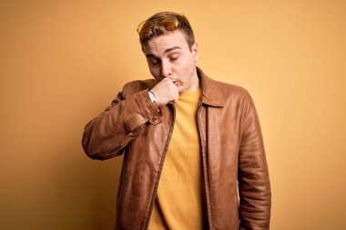 Sarı arka planda rahat deri ceket giyen genç ve yakışıklı bir adam kendini iyi hissetmiyor ve soğuk algınlığı veya bronşitin belirtisi olarak öksürüyor. Sağlık hizmeti kavramı.
